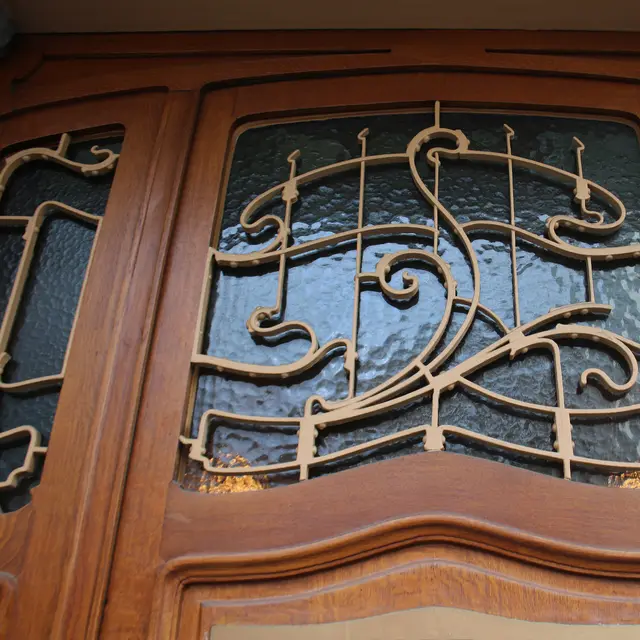 A carved wooden front door with curling iron grilles over its glass