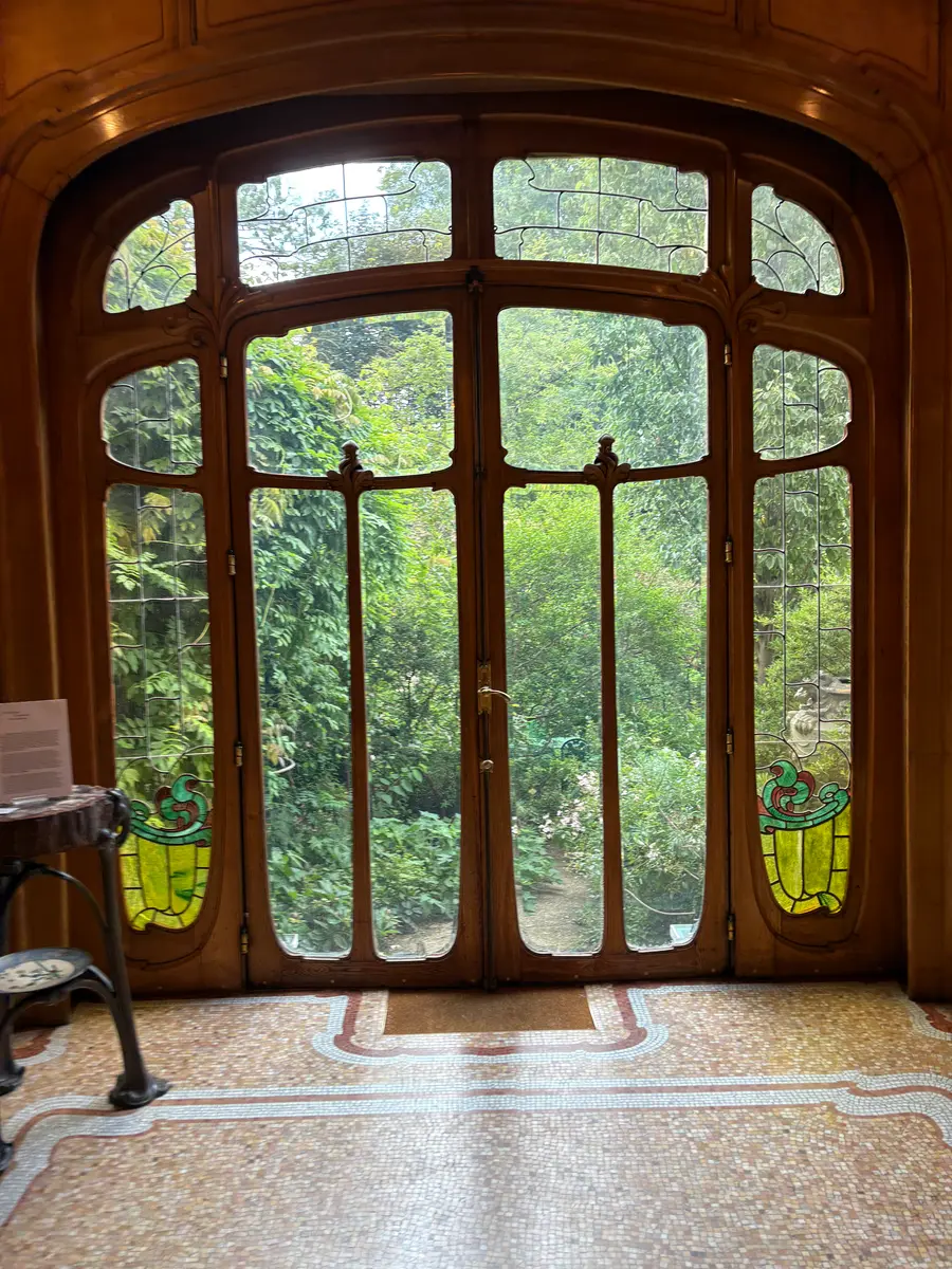 Tall glazed double doors in curving wooden frames opening onto green garden, above a mosaic floor